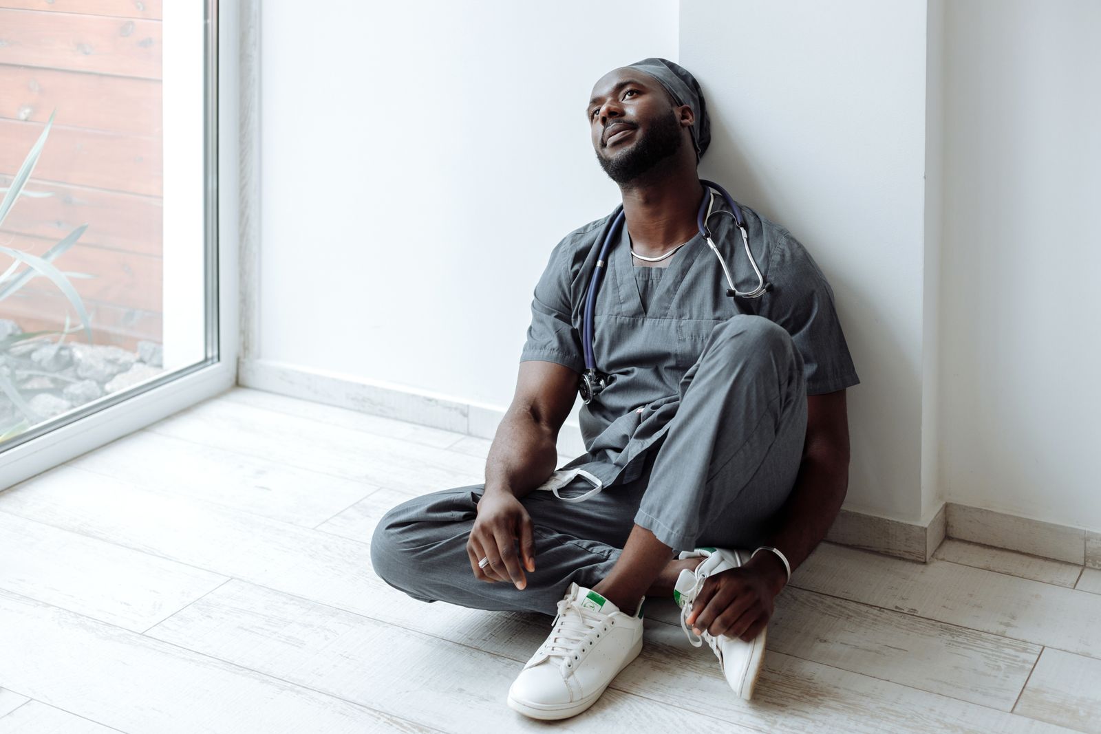 A clinician in scrubs taking a moment on the floor of a quiet corridor